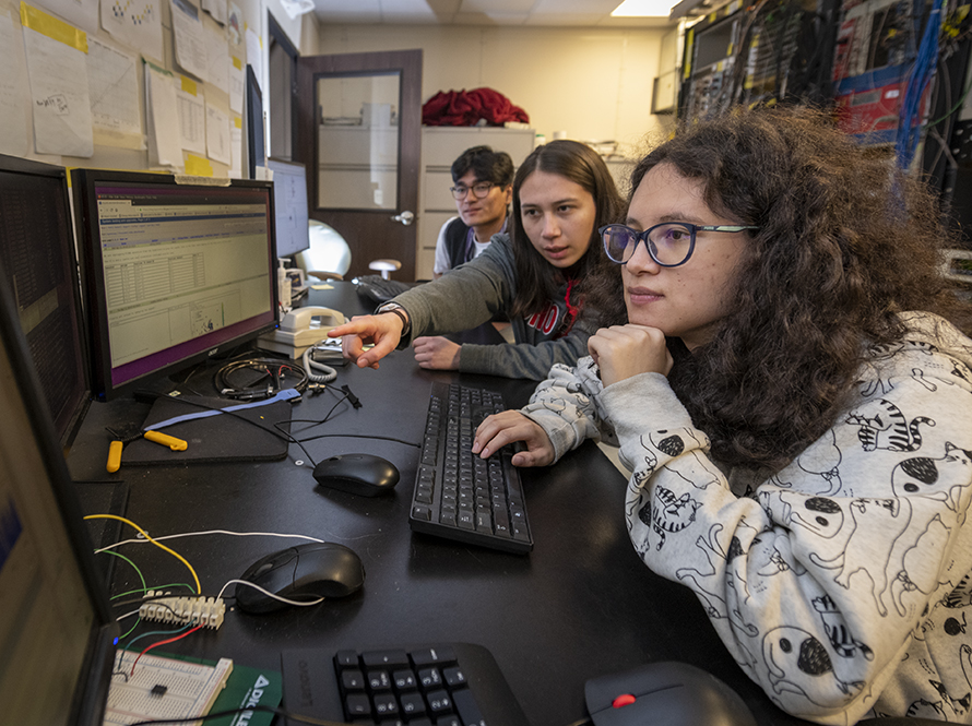 Three undergraduate interns working together at a desk with several computers