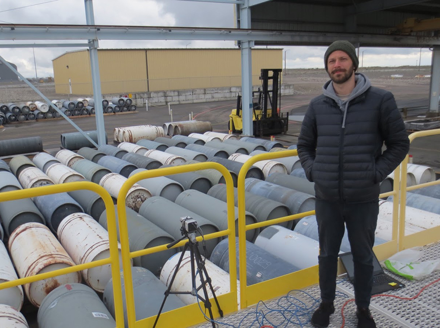LBNL Scientist Daniel Hellfeld and H3D detector (mounted on tripod) in front of the Type-30B UF6 cylinder storage yard.
