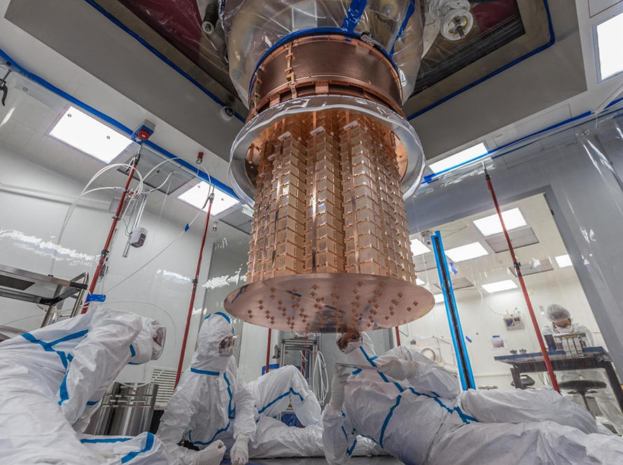 Three researchers in clean-room suits on the floor working on the CUORE detector.