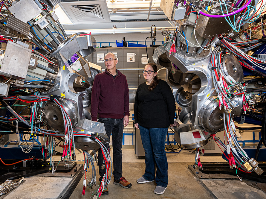 Two people surrounded by a large aluminum sphere with dozens of cables.