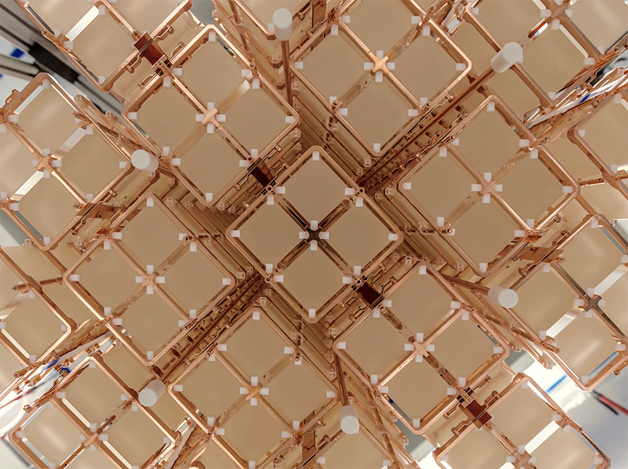 Close-up view of an array of cubic, pale crystals held in a copper framework. The structure is composed of multiple repeating units arranged in a symmetrical, grid-like pattern, with small white spacers at the intersections.