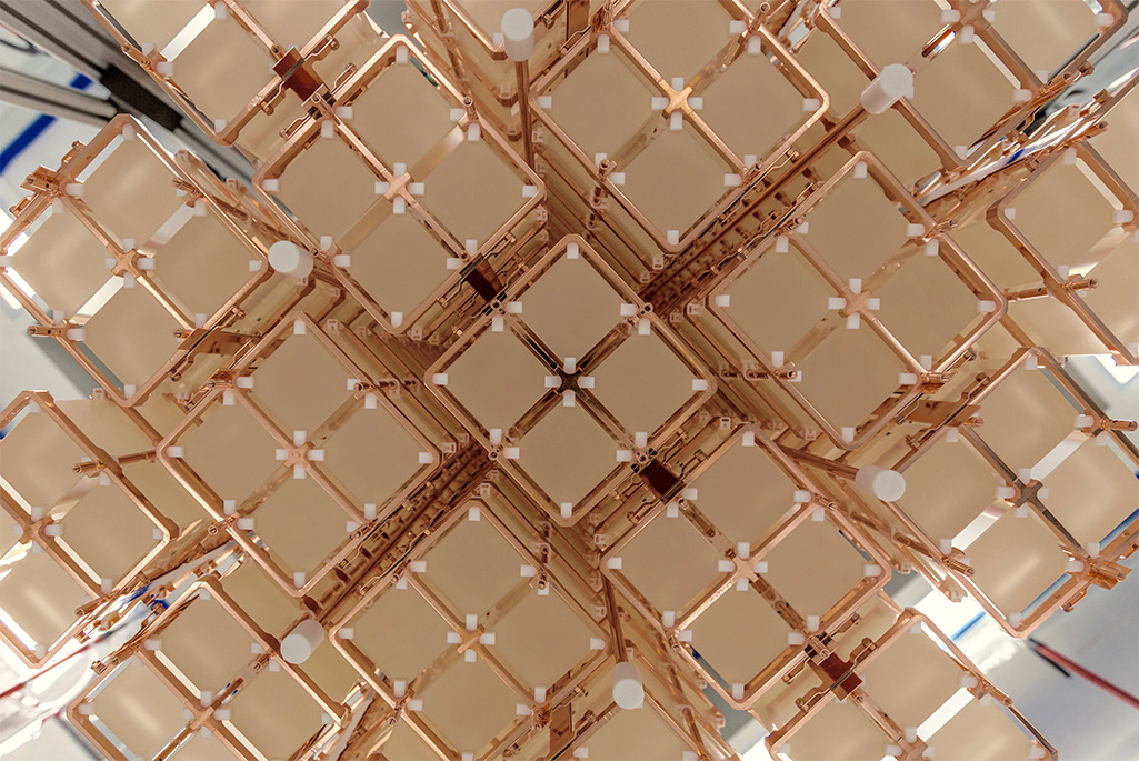 Close-up view of an array of cubic, pale crystals held in a copper framework. The structure is composed of multiple repeating units arranged in a symmetrical, grid-like pattern, with small white spacers at the intersections.