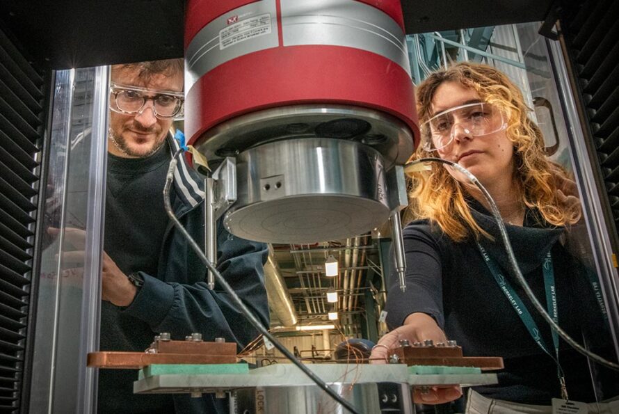 Two researchers in protective glasses look into a superconducting magnet experimental setup.