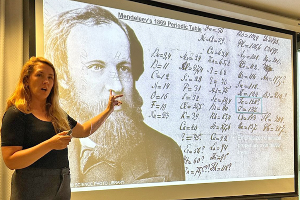 A blond white woman stands in front of a projected image.