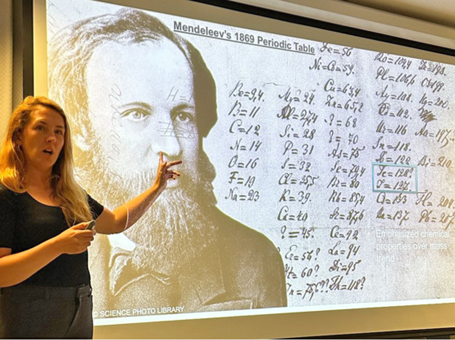 A blond white woman stands in front of a projected image.