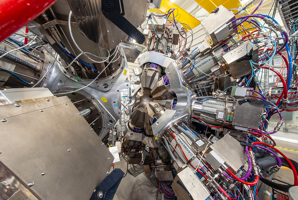 Close-up of GRETA’s two separated halves, showing germanium detector modules arranged around a central opening and surrounded by dense bundles of multicolored wiring and tubing.